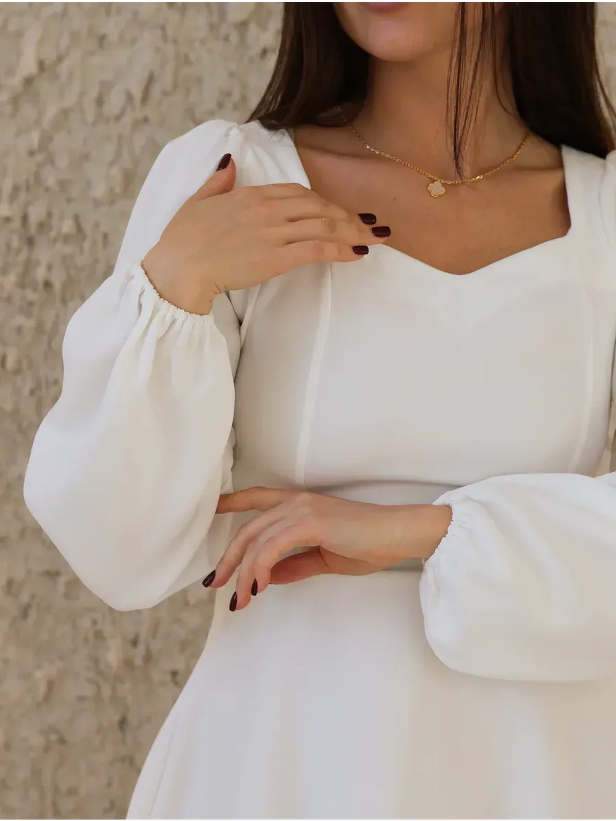 Close-up of a woman wearing an ivory structured dress with a sweetheart neckline and puff sleeves, perfect for wedding guest or formal occasions.