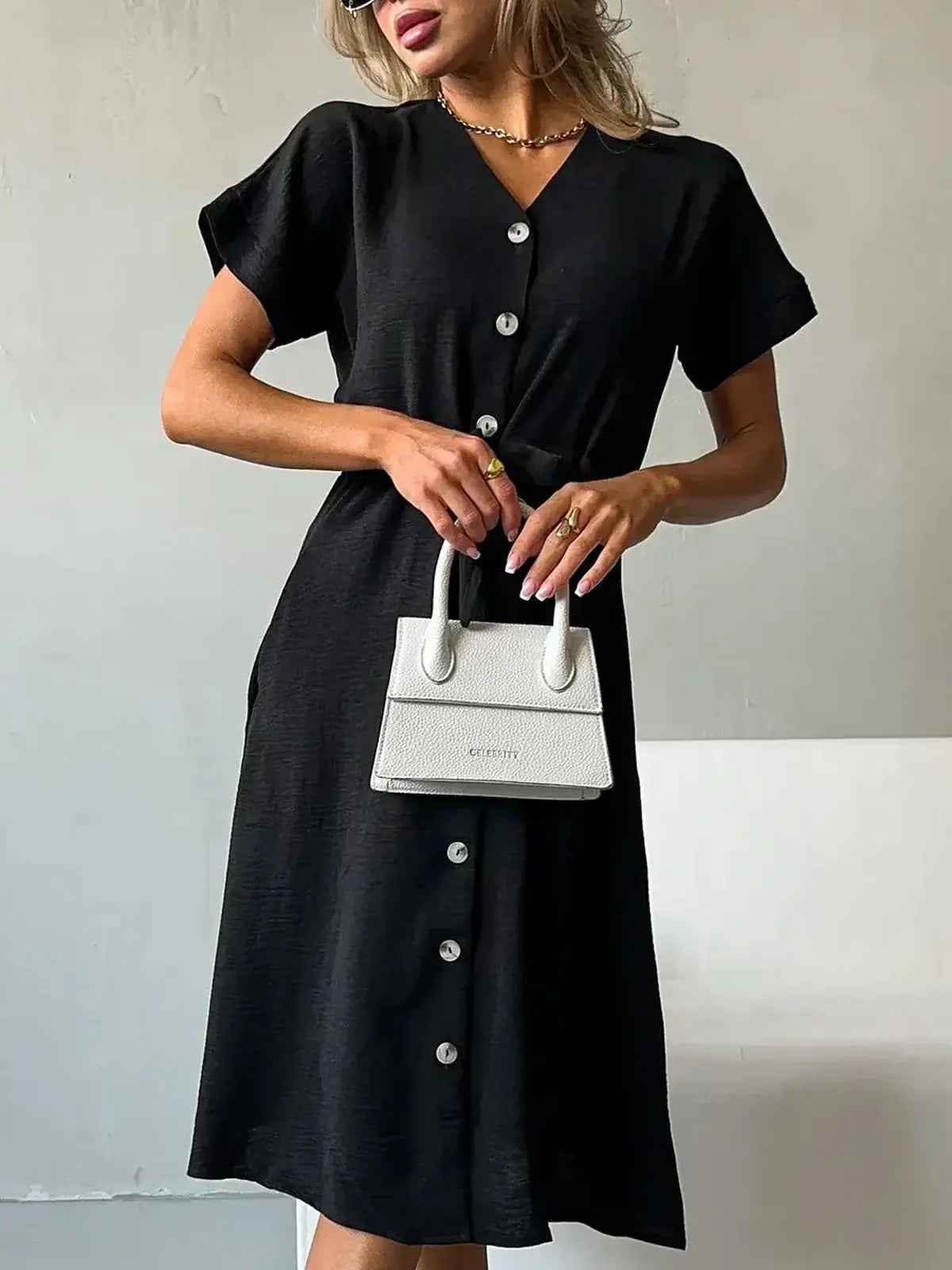 Model showcasing the Iconic Ease Midi Dress in black with button-front design and stylish white handbag.
