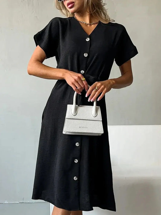Model showcasing the Iconic Ease Midi Dress in black with button-front design and stylish white handbag.