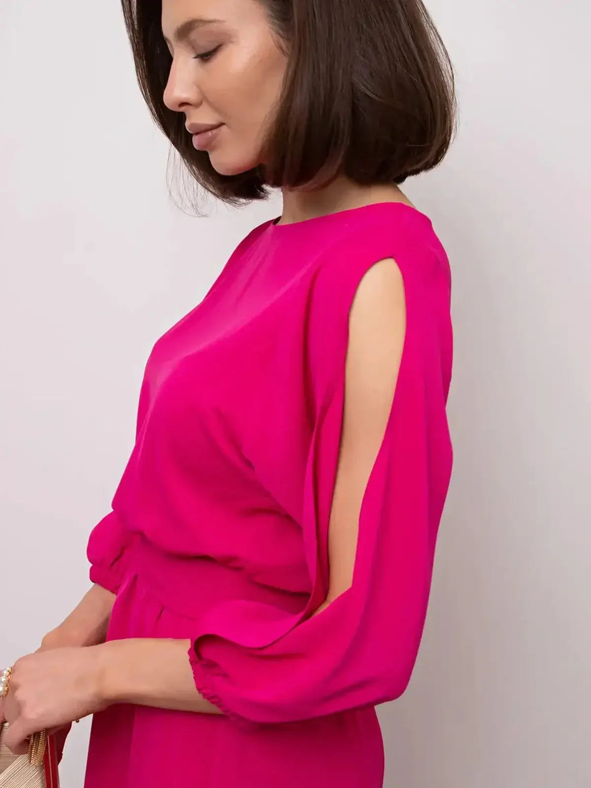 Side view of a woman in a vibrant fuchsia midi dress with shoulder cutouts, showcasing elegance and style.