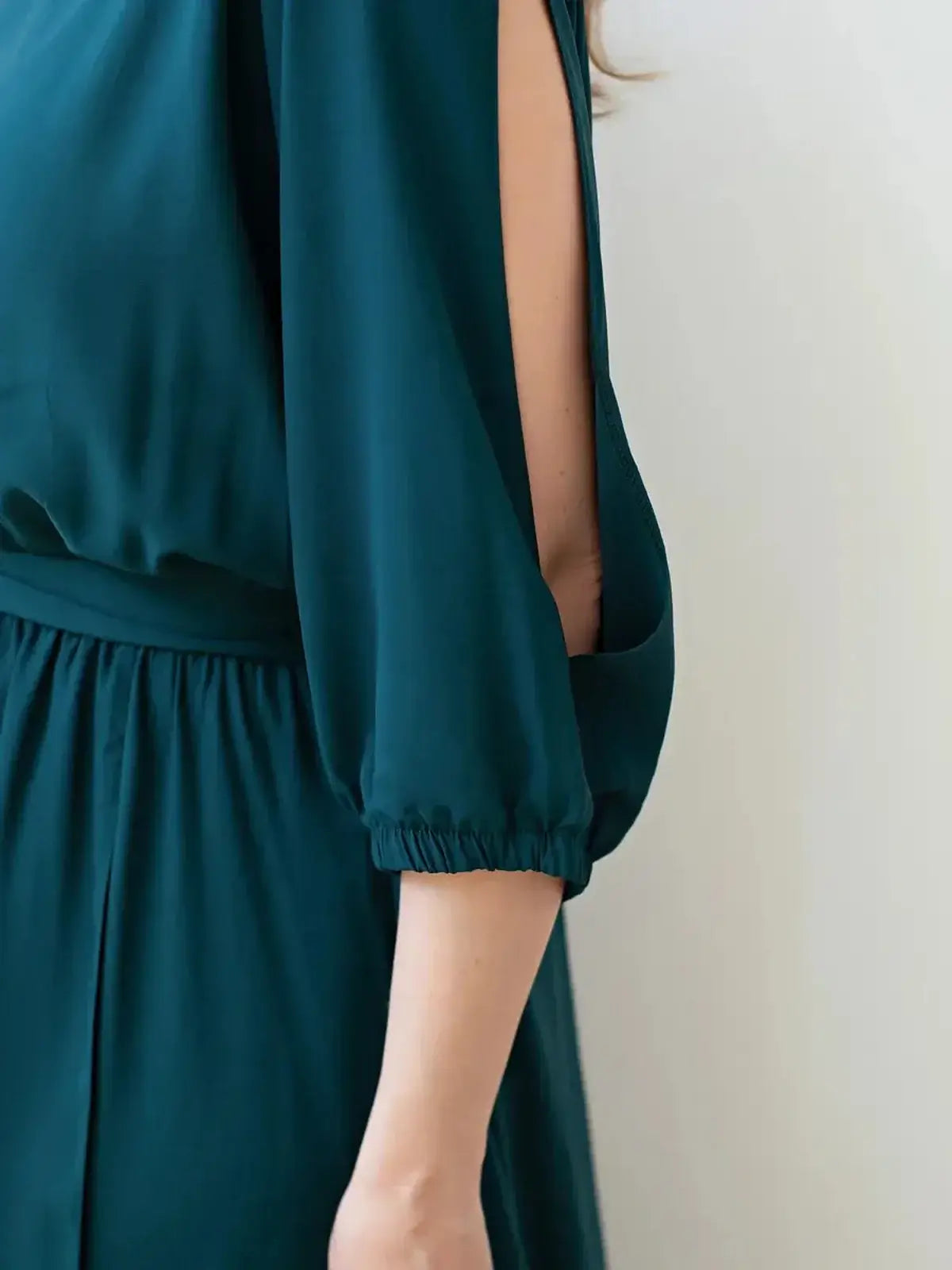 Close-up of Cascade Midi Dress showcasing elegant shoulder cutouts and draped sleeves in a deep teal color.