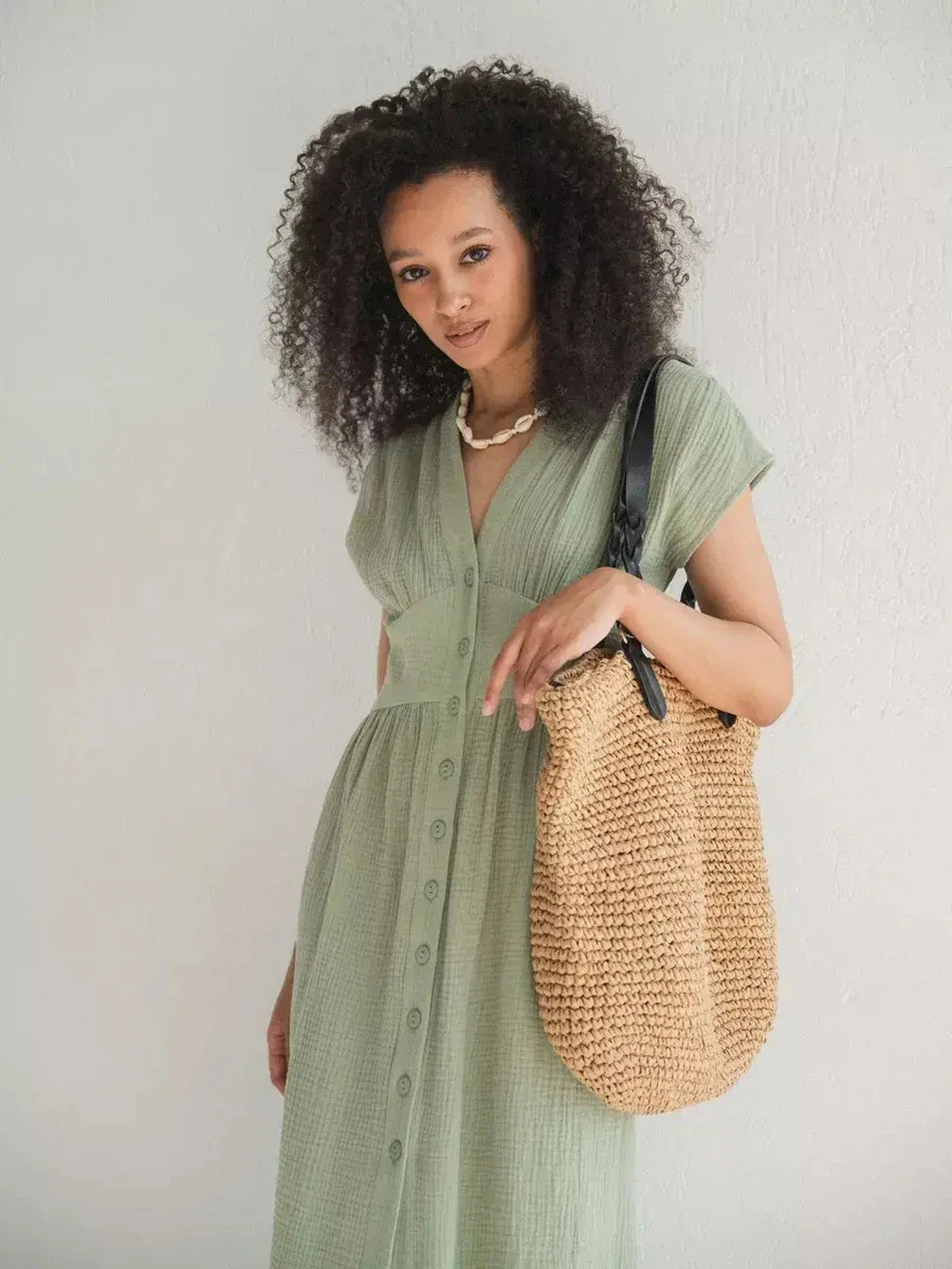 Model wearing a lightweight khaki midi dress with a V-neckline, complemented by a stylish woven bag.
