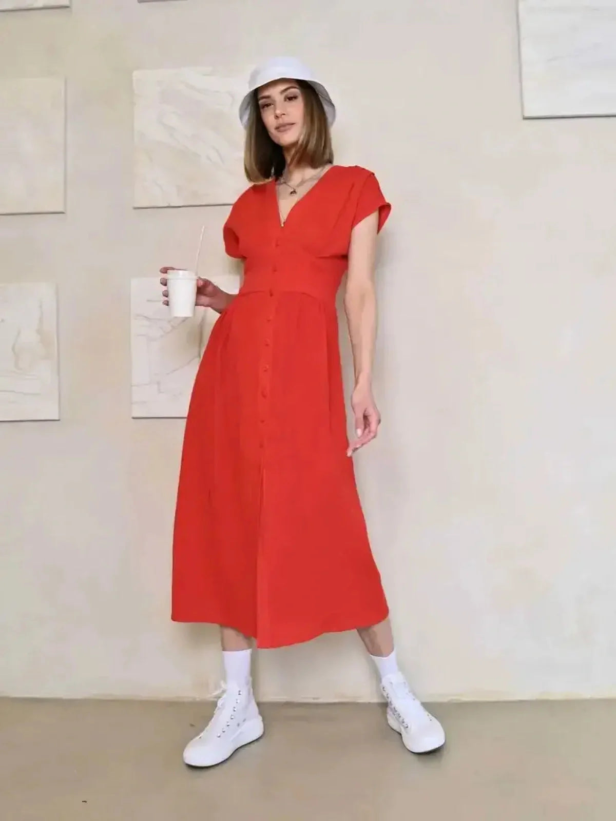 Model in a red midi dress with V-neck and button detail, styled casually with white sneakers and a hat.