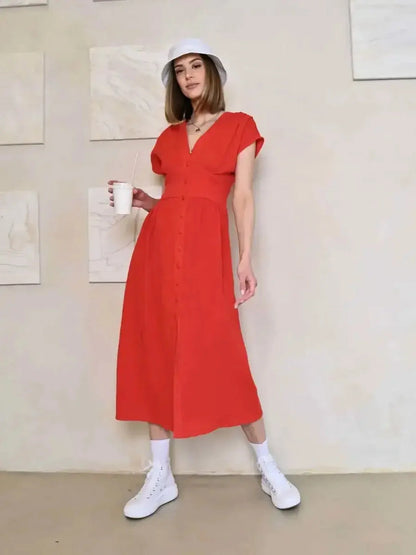 Model in a red midi dress with V-neck and button detail, styled casually with white sneakers and a hat.