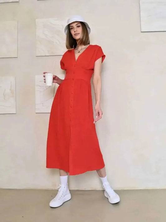 Model in a red midi dress with V-neck and button detail, styled casually with white sneakers and a hat.