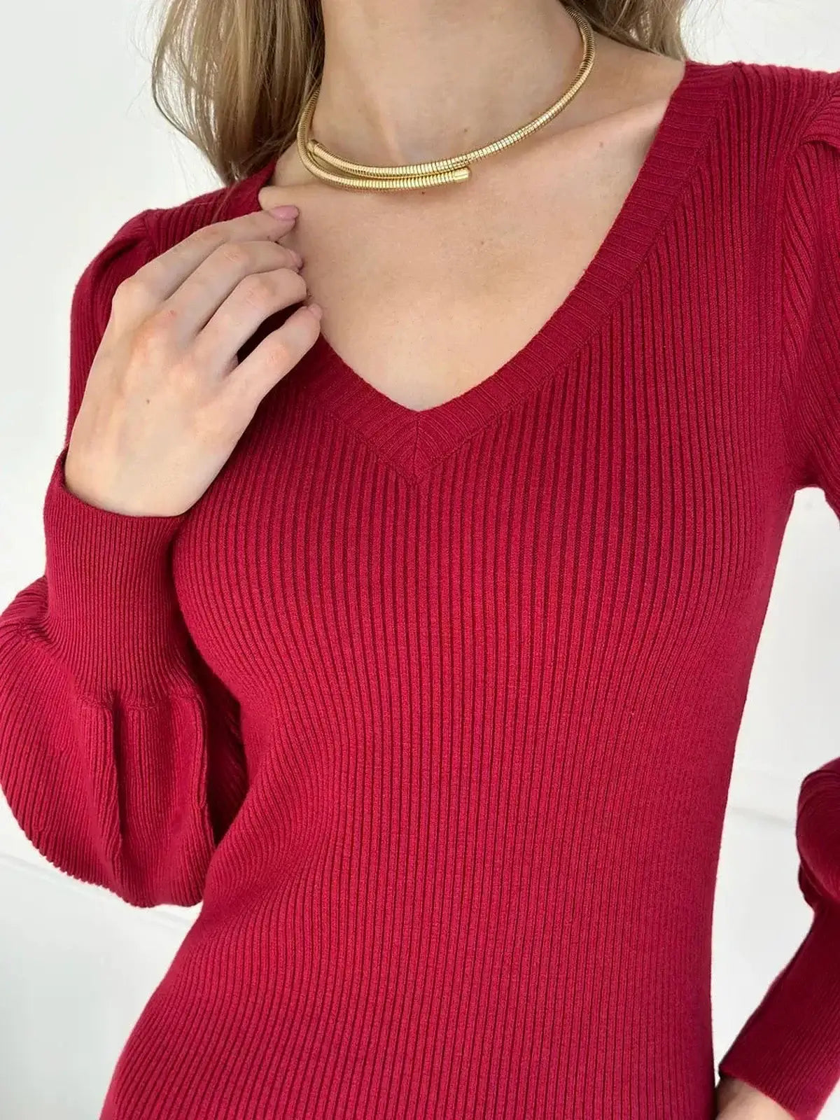 Close-up of a woman wearing a ribbed red midi dress with a V-neckline and gold necklace, showcasing elegance and femininity.