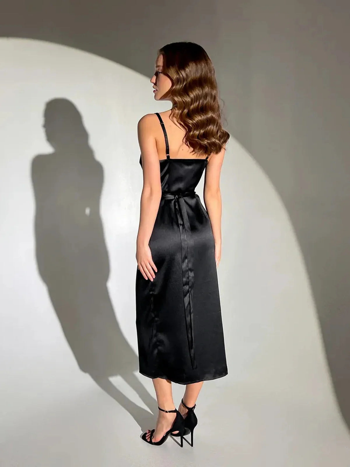 Elegant woman in a black satin midi dress showcasing a flattering wrap silhouette and chic design.