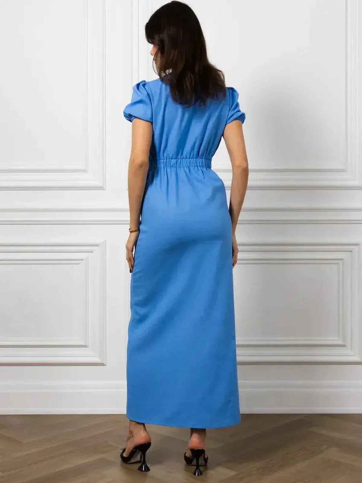Back view of a woman wearing the Maxi Dress Azure Charm in sky blue, featuring a cinched waist and short puff sleeves.