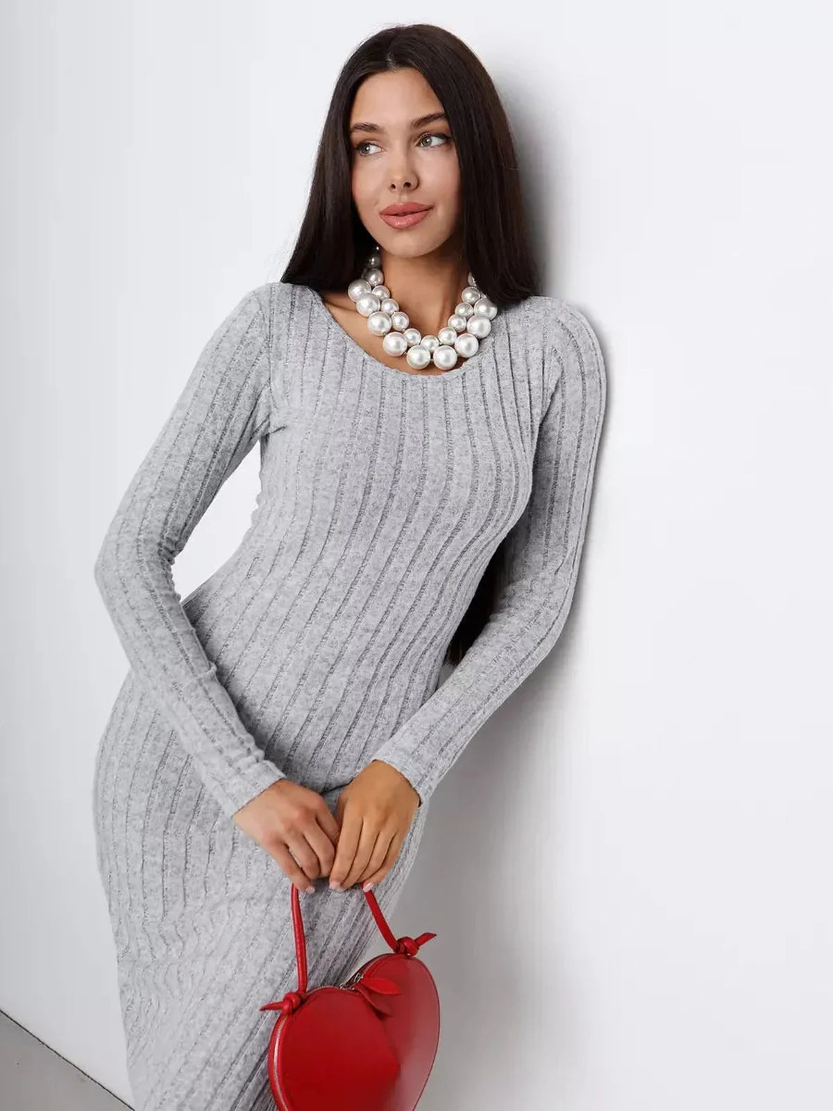 Elegant woman in a ribbed gray midi dress with pearl necklace and red handbag, showcasing sophisticated style.