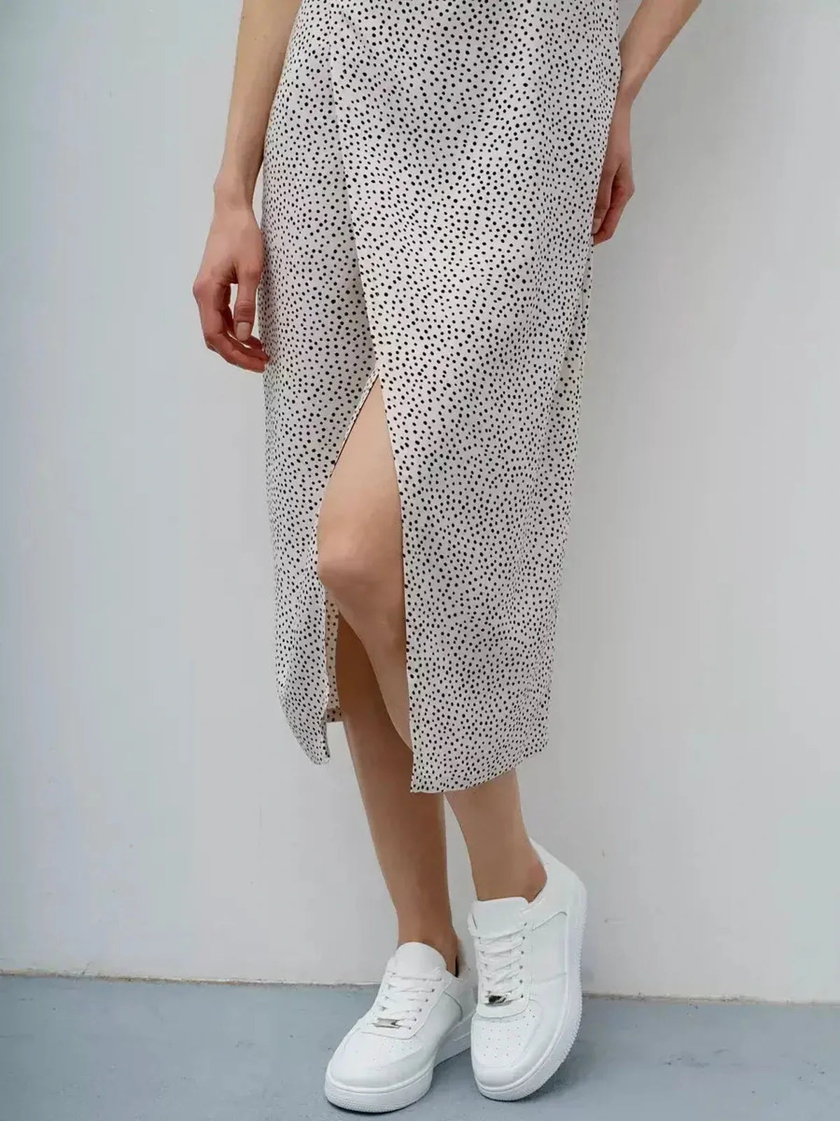 Model wearing the Dot Whisper Midi Dress with playful polka dot print, paired with stylish white sneakers.