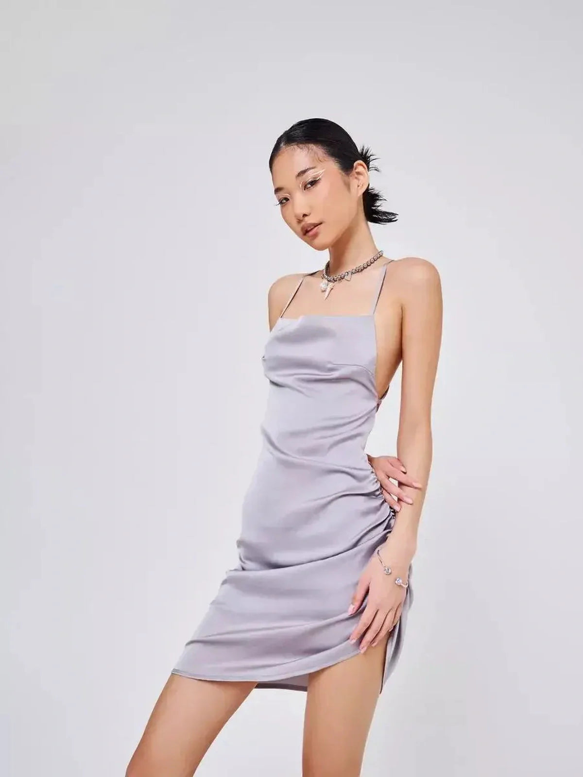 Mini dress in silver-gray satin with sultry ruching and crisscross straps, ideal for summer soirées and formal events.