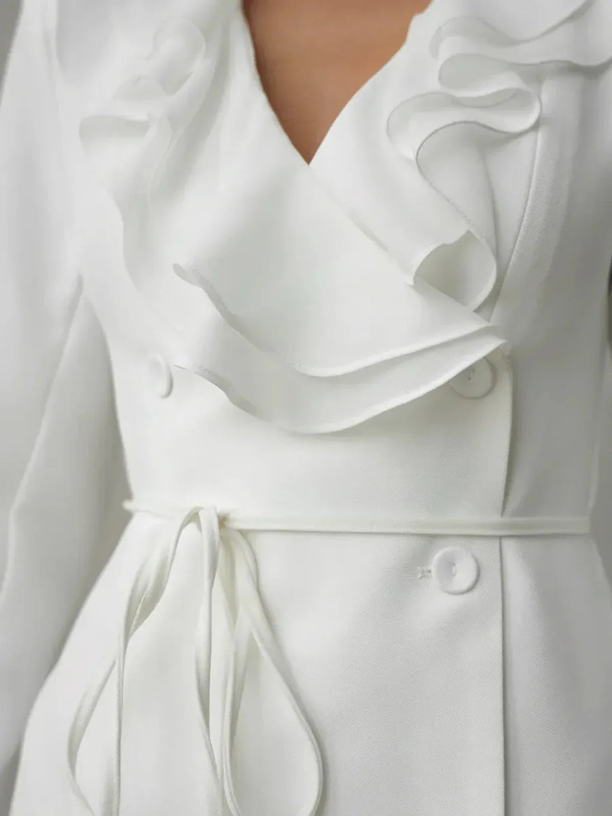 Close-up of a white long sleeve dress featuring statement ruffles and a deep V-neckline, ideal for modern wedding guest looks.