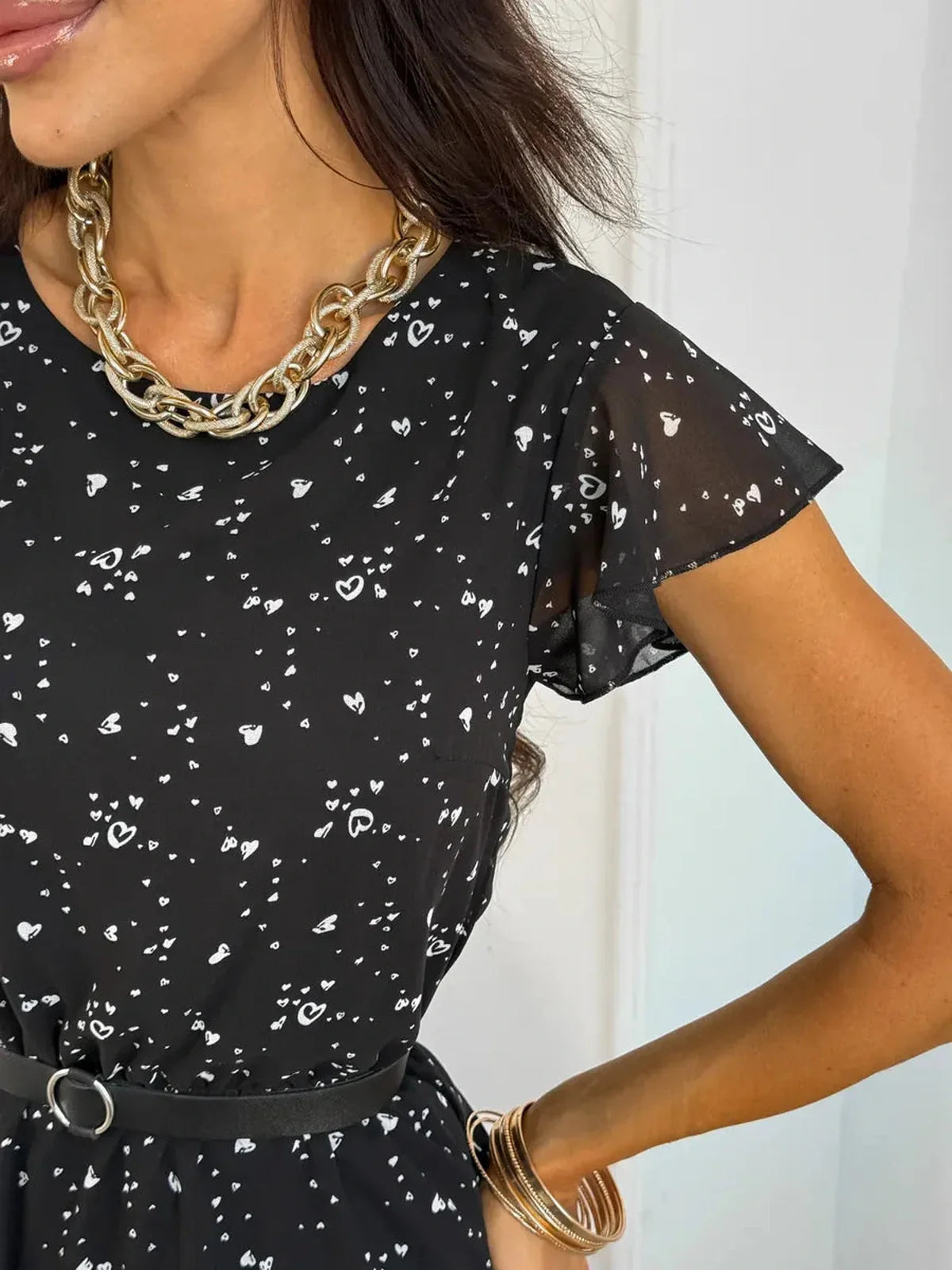 Close-up of a woman wearing the Midnight Dots Mini Dress featuring flutter sleeves and a chic belt, accessorized with a bold necklace.