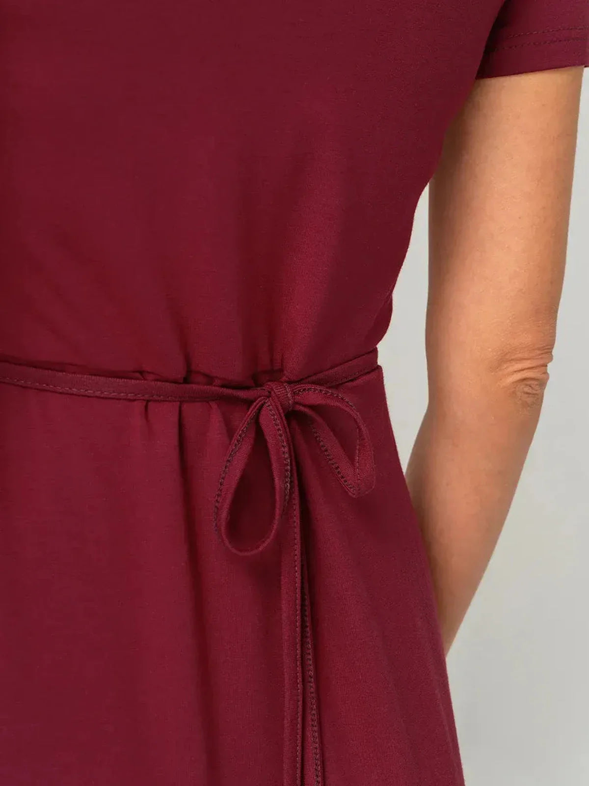 Close-up of the tie waist detail on a deep red wrap mini dress, showcasing its elegant draped style.