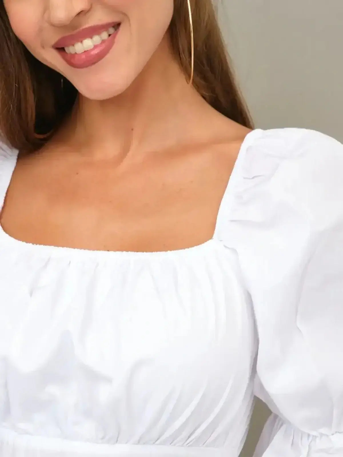 Close-up of a woman's upper body wearing a white dress with puff sleeves and a square neckline, radiating summer elegance.