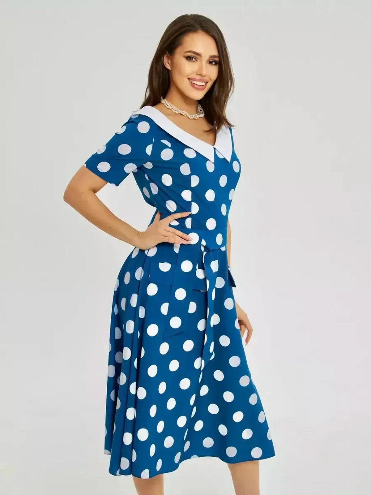 Model showcasing a Pearl Dot Midi Dress with oversized white polka dots, white collar, and tie waist in dark teal.