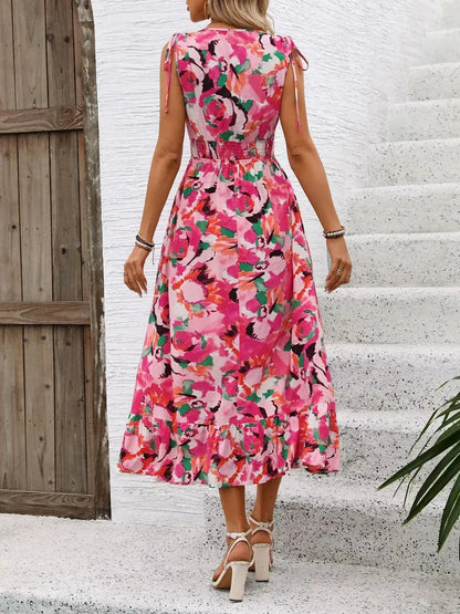 Back view of a woman in a vibrant pink floral midi dress with strappy details, perfect for summer occasions.