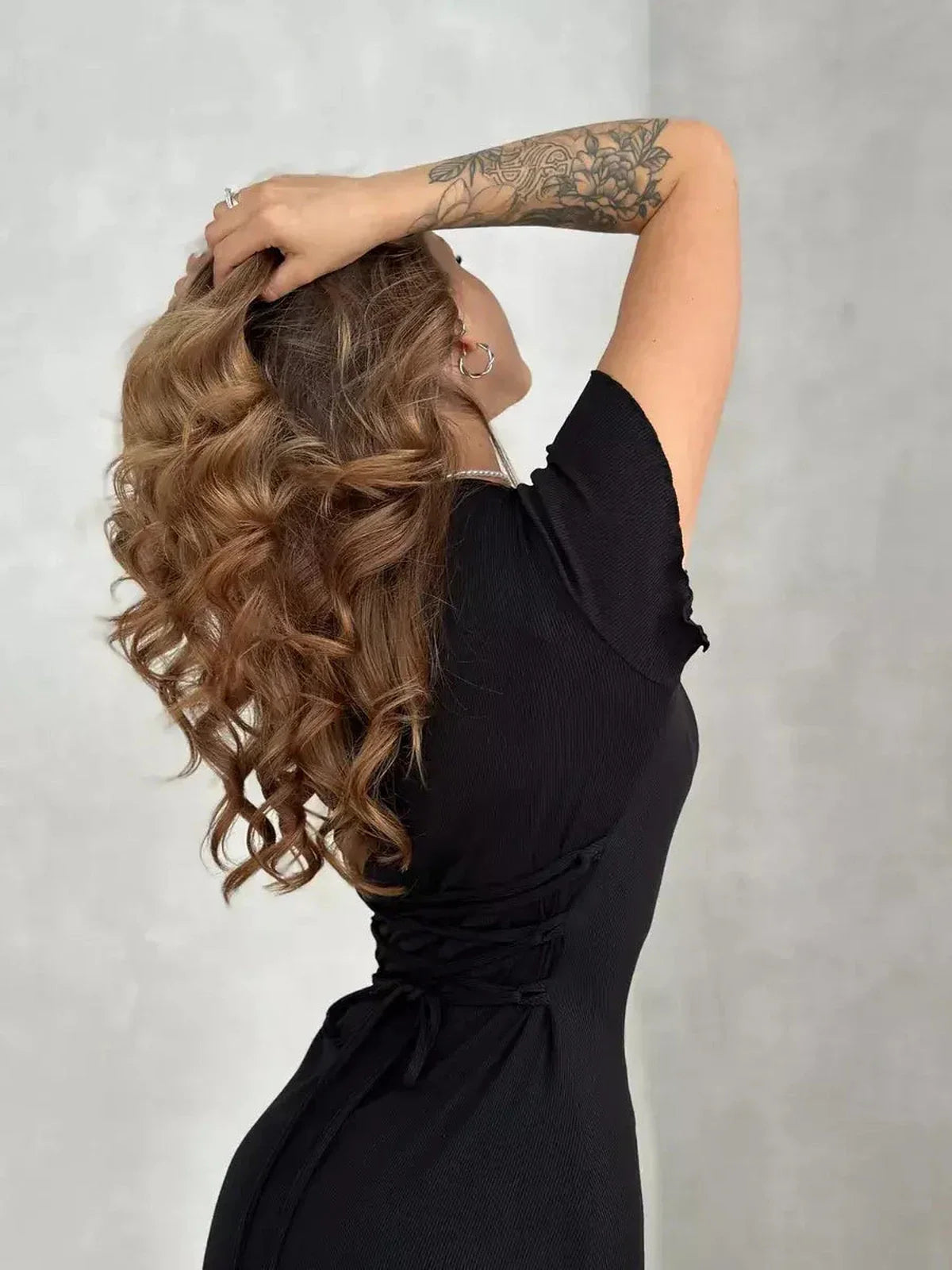 Model showcasing the Laced Icon Mini Dress with a lace-up back, featuring flowing curls and a stylish black silhouette.