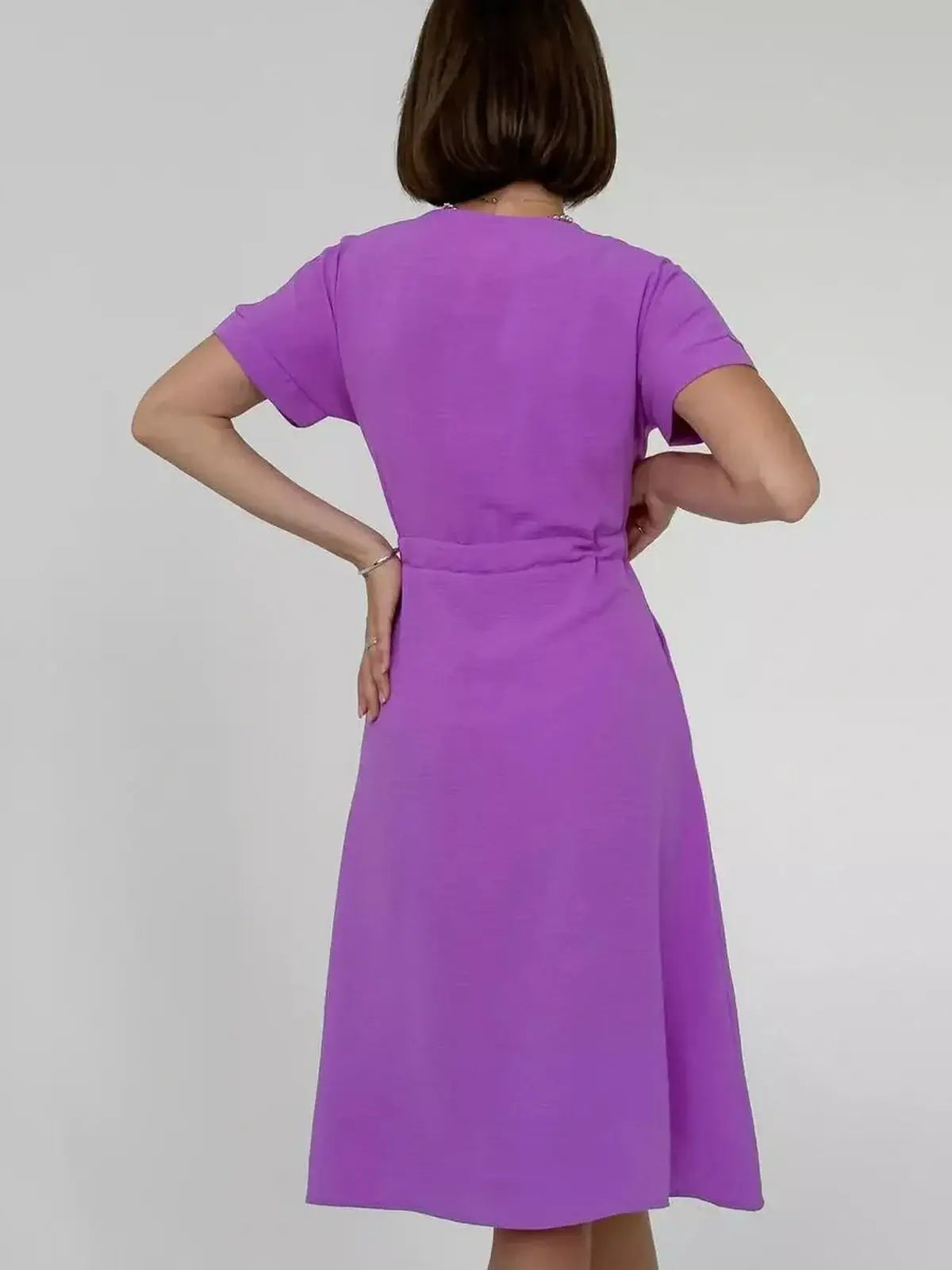 Woman in a lavender midi dress showcasing a breezy fit and structured design, featuring short sleeves and a waist cinching tie.