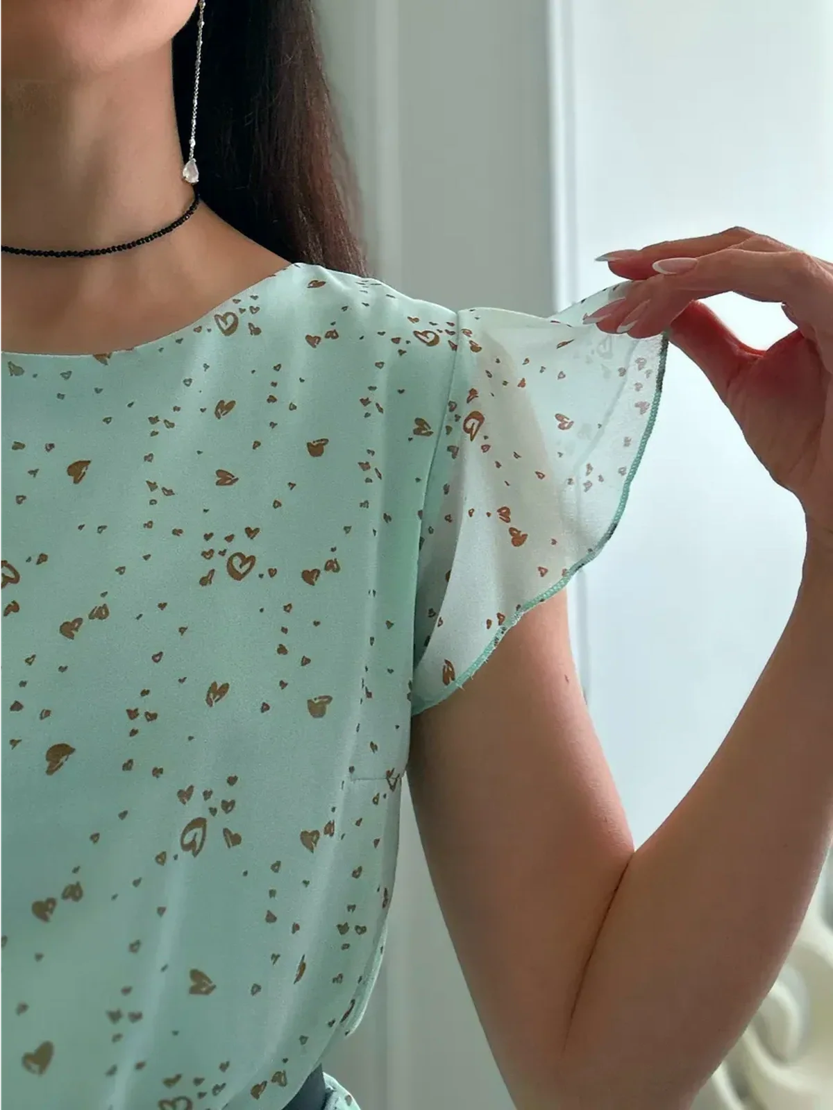 Close-up of a mint chiffon mini dress with fluttery sleeves and a delicate heart print, perfect for summer occasions.