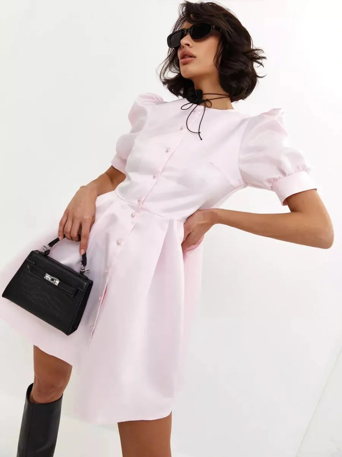 Woman wearing a Pearl Puff Mini Dress in pink with puff sleeves, paired with sunglasses and a black handbag.