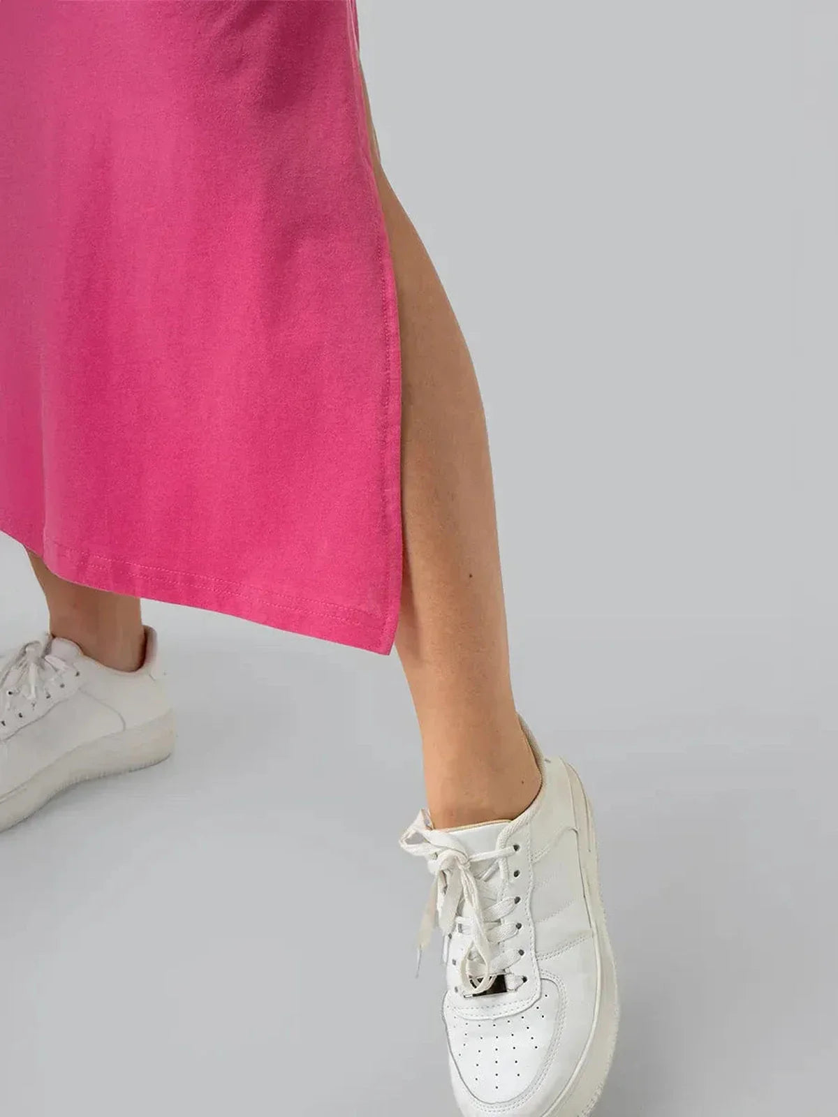 Close-up of a woman’s leg wearing a pink midi dress with side slit and white sneakers.