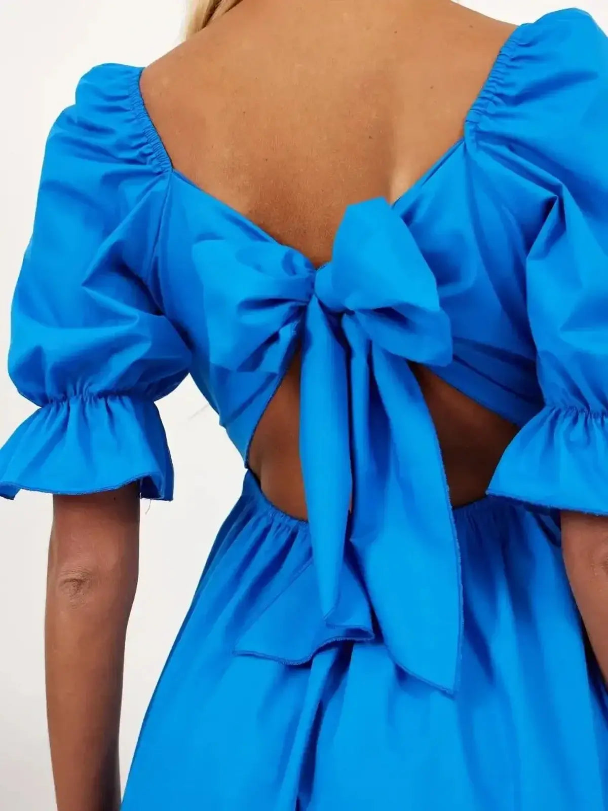 Back view of vibrant blue mini dress with a dramatic bow tie closure, perfect for summer occasions.