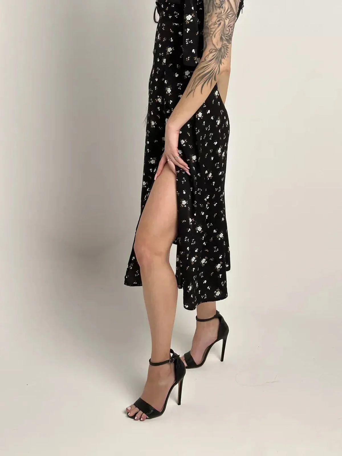 Elysian Midi Dress in elegant black floral print, featuring a side slit and paired with stylish high heels.