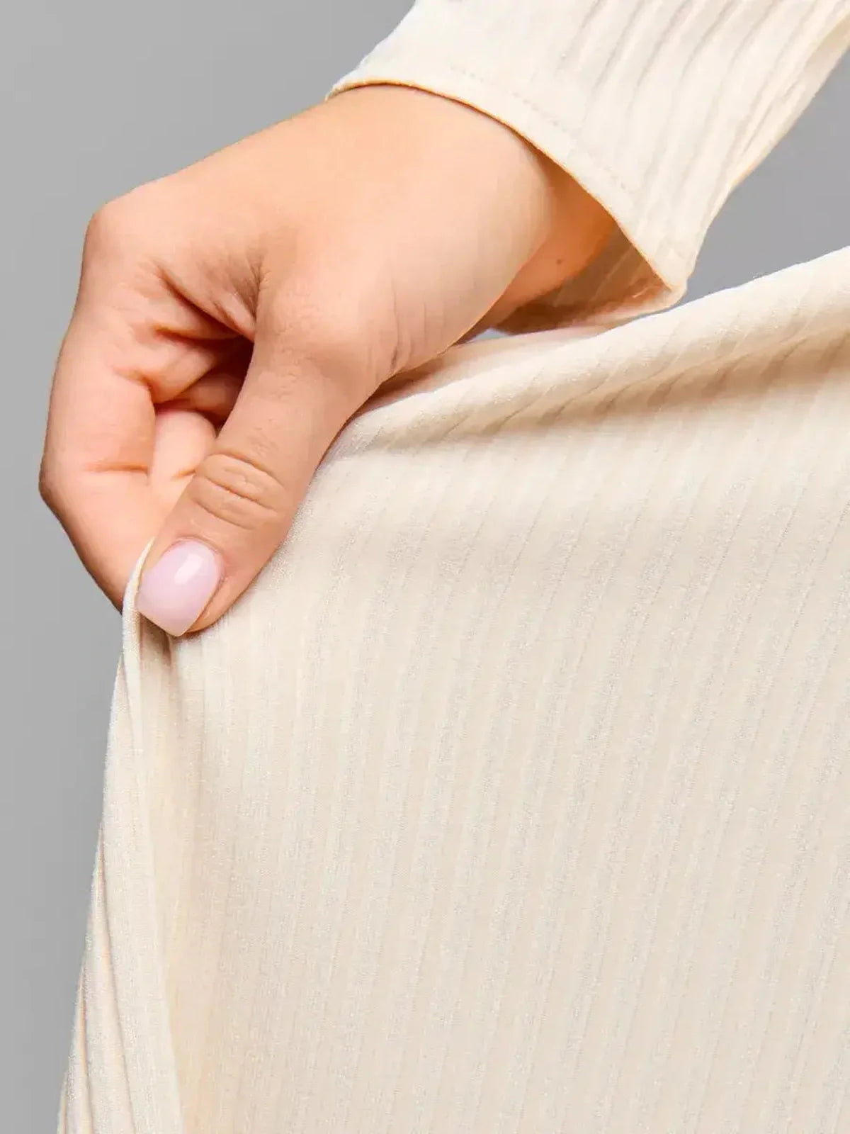 Close-up of a hand gently holding the soft ribbed texture of a cream midi dress, highlighting its elegance and comfort.