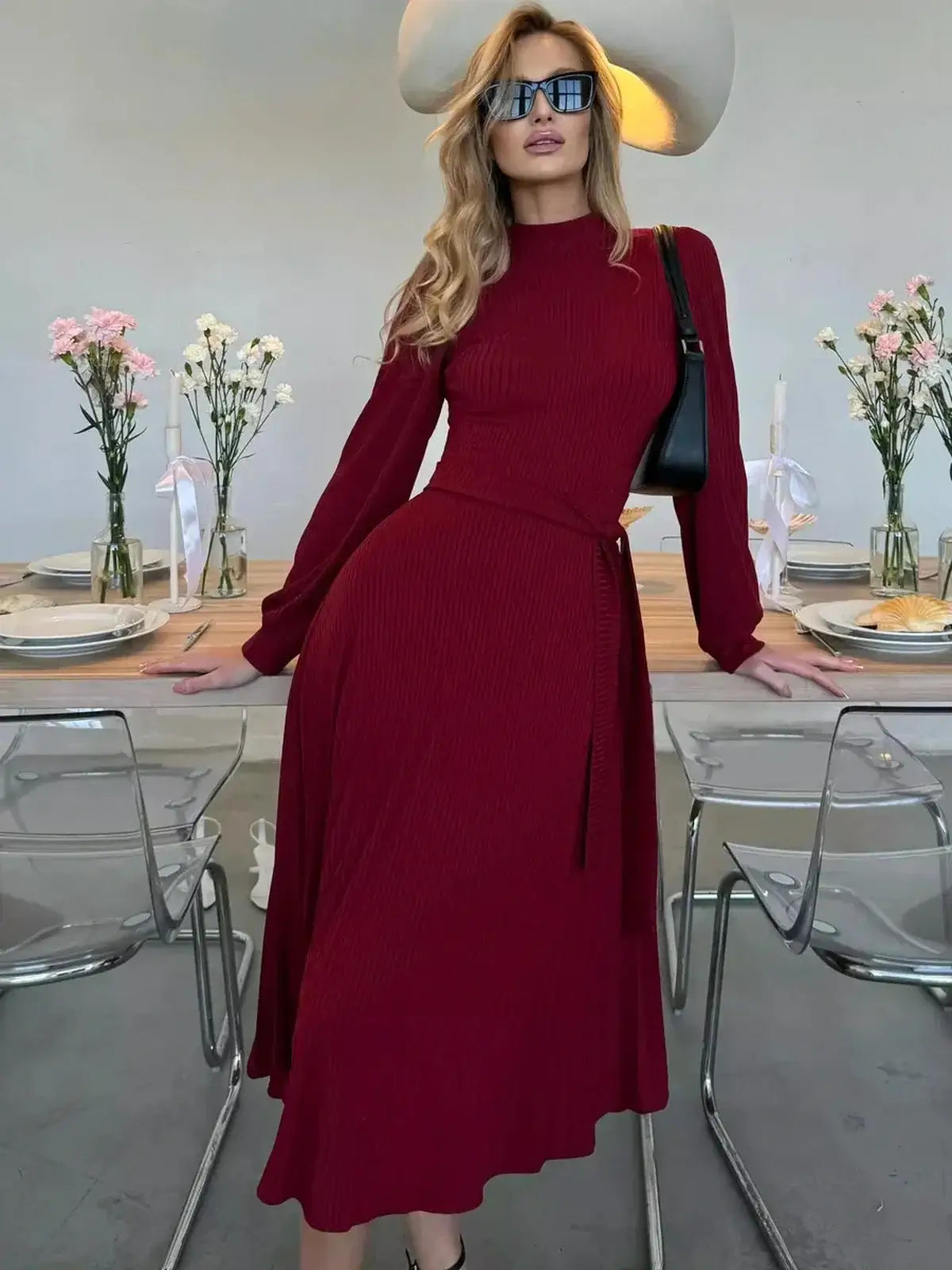 Model showcasing the Crimson Grace Midi Dress in rich red, featuring pleats and a sculpted knit at a stylish table setting.