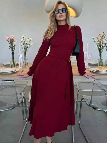 Model showcasing the Crimson Grace Midi Dress in rich red, featuring pleats and a sculpted knit at a stylish table setting.