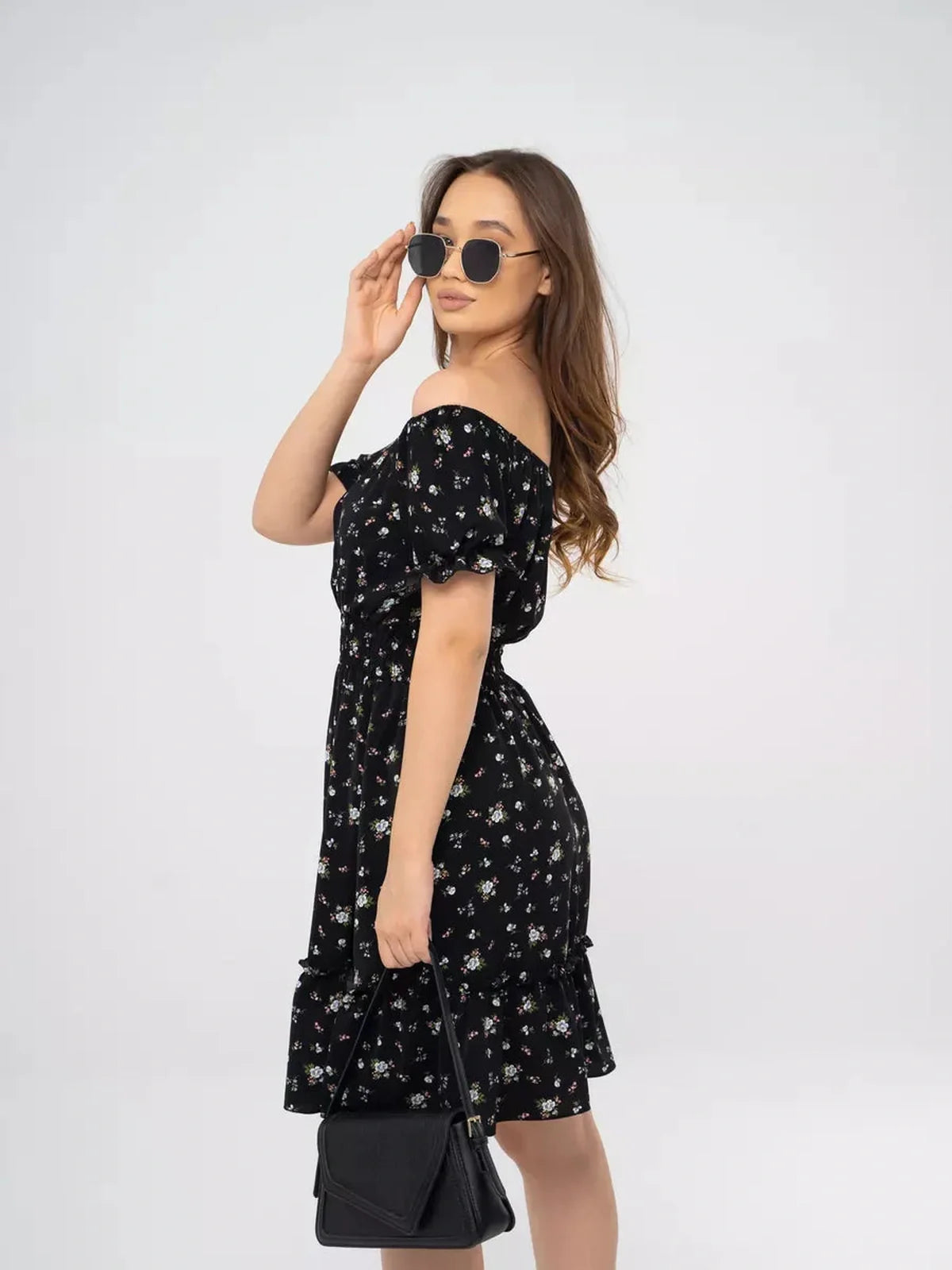 Model showcasing the Midnight Bloom black mini dress with floral print, off-shoulder style, and playful tiered skirt.