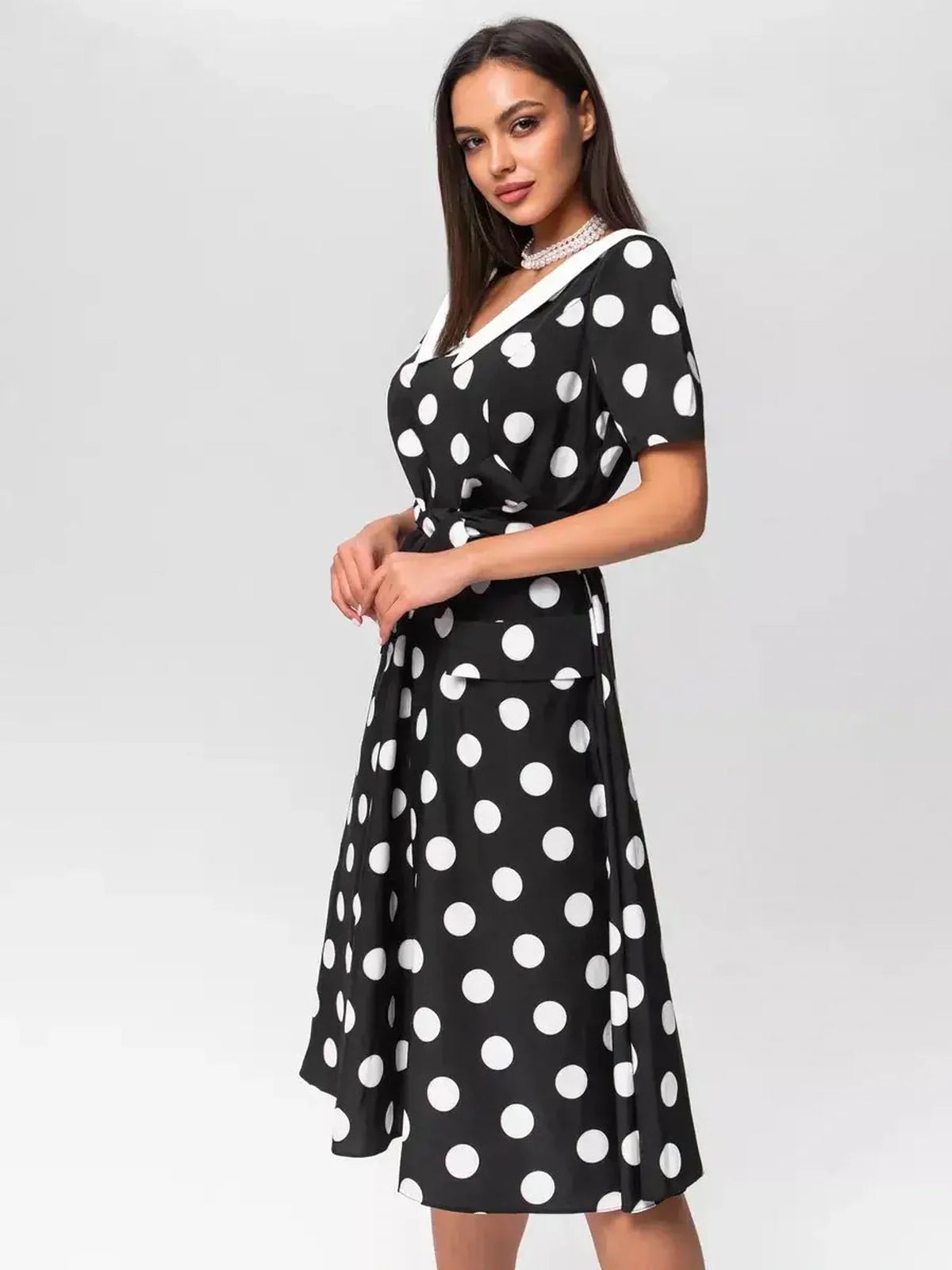 Elegant black-and-white polka dot midi dress with V-neckline and waist tie, perfect for summer occasions.