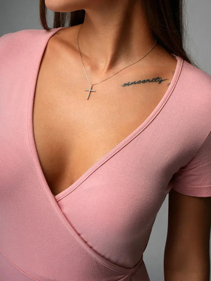 Close-up of a woman wearing a blush wrap mini dress with a deep V-neckline, showcasing a necklace and tattoo on her collarbone.