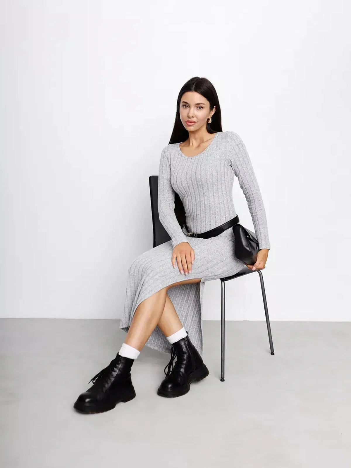 Model wearing a Soft Curve Midi Dress in grey, featuring a ribbed design and casual black boots, seated on a chair.