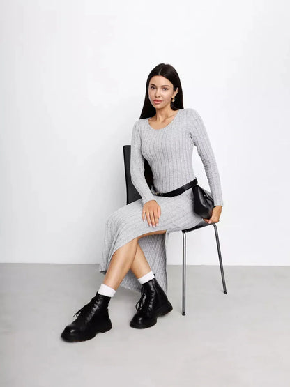 Model wearing a Soft Curve Midi Dress in grey, featuring a ribbed design and casual black boots, seated on a chair.