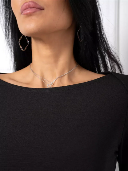Close-up of a woman wearing a black dress with a boat neckline, paired with elegant earrings and necklace.