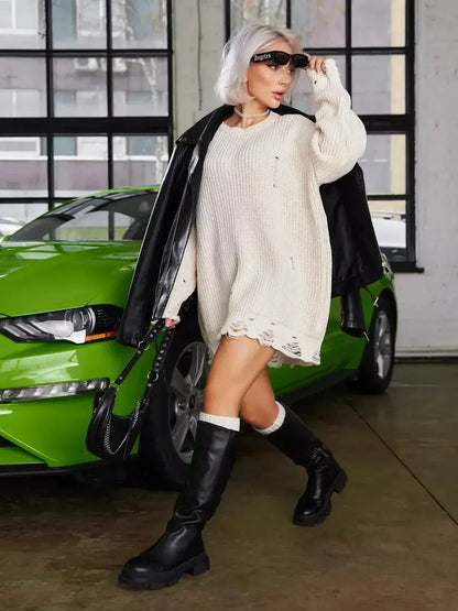 Model in oversized ivory knit mini dress with raw-cut details and black knee-high boots, posing next to a green car.