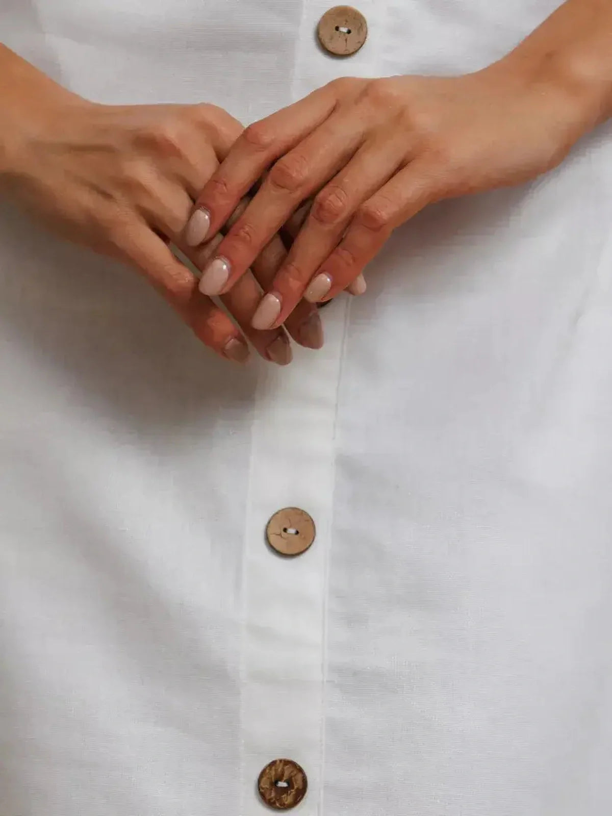 Close-up of hands on a white maxi dress featuring rustic wooden buttons.