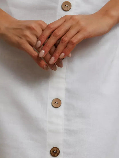 Close-up of hands on a white maxi dress featuring rustic wooden buttons.