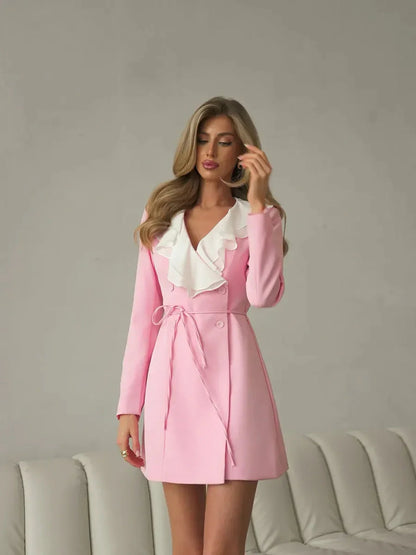 Stylish woman in a blush pink Rose Cascade mini dress with a dramatic white ruffle neckline and wrap silhouette.