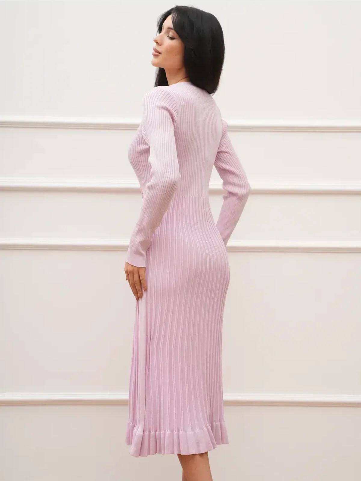 Woman wearing a crystal knit midi dress in soft pink, showcasing a ribbed texture and fluted hem.