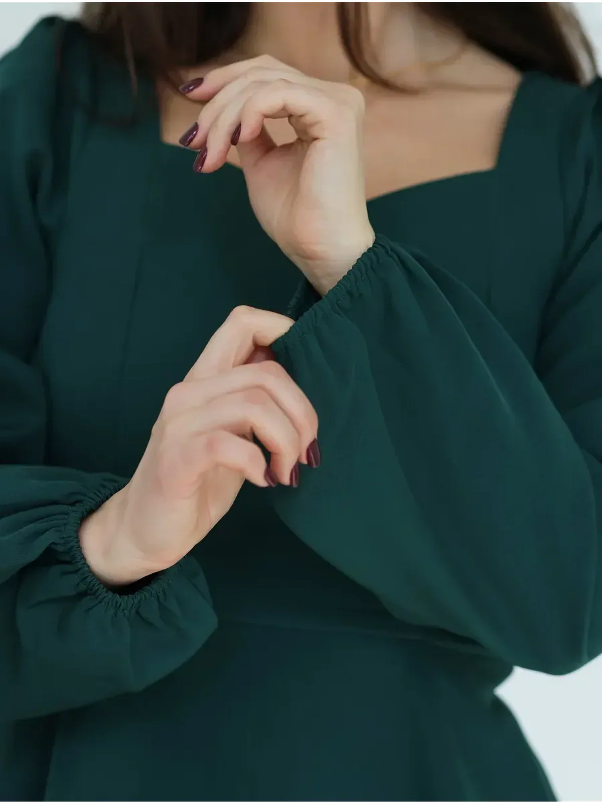 Close-up of hands showcasing the puff sleeves and sculpted bodice of an elegant emerald green mini dress.