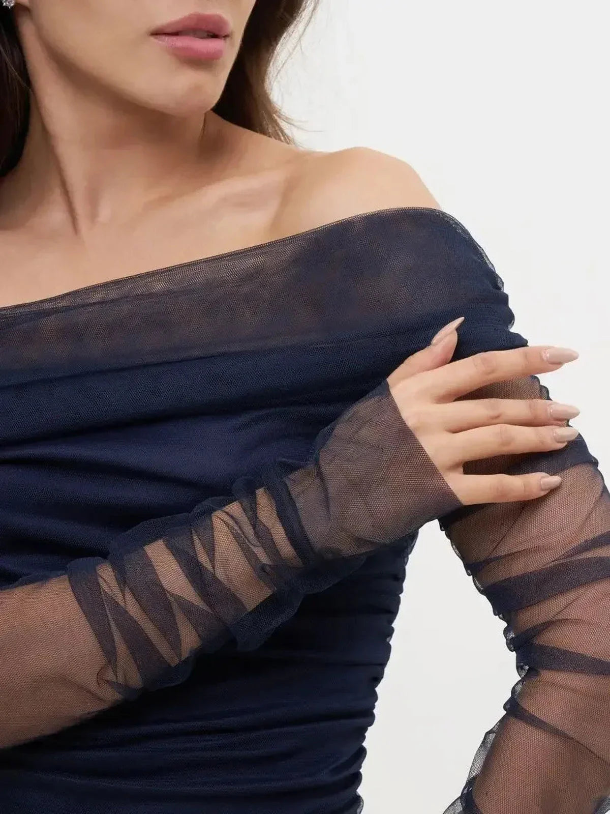 Close-up of a model's off-shoulder navy mesh midi dress, showcasing ruched fabric and sheer long sleeves.