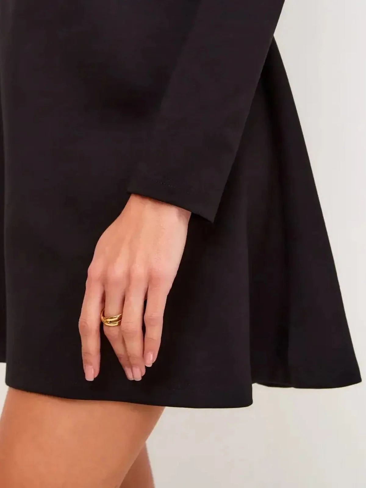 Detail of a woman wearing a sleek black dress showcasing a flared skirt and elegant long sleeves.