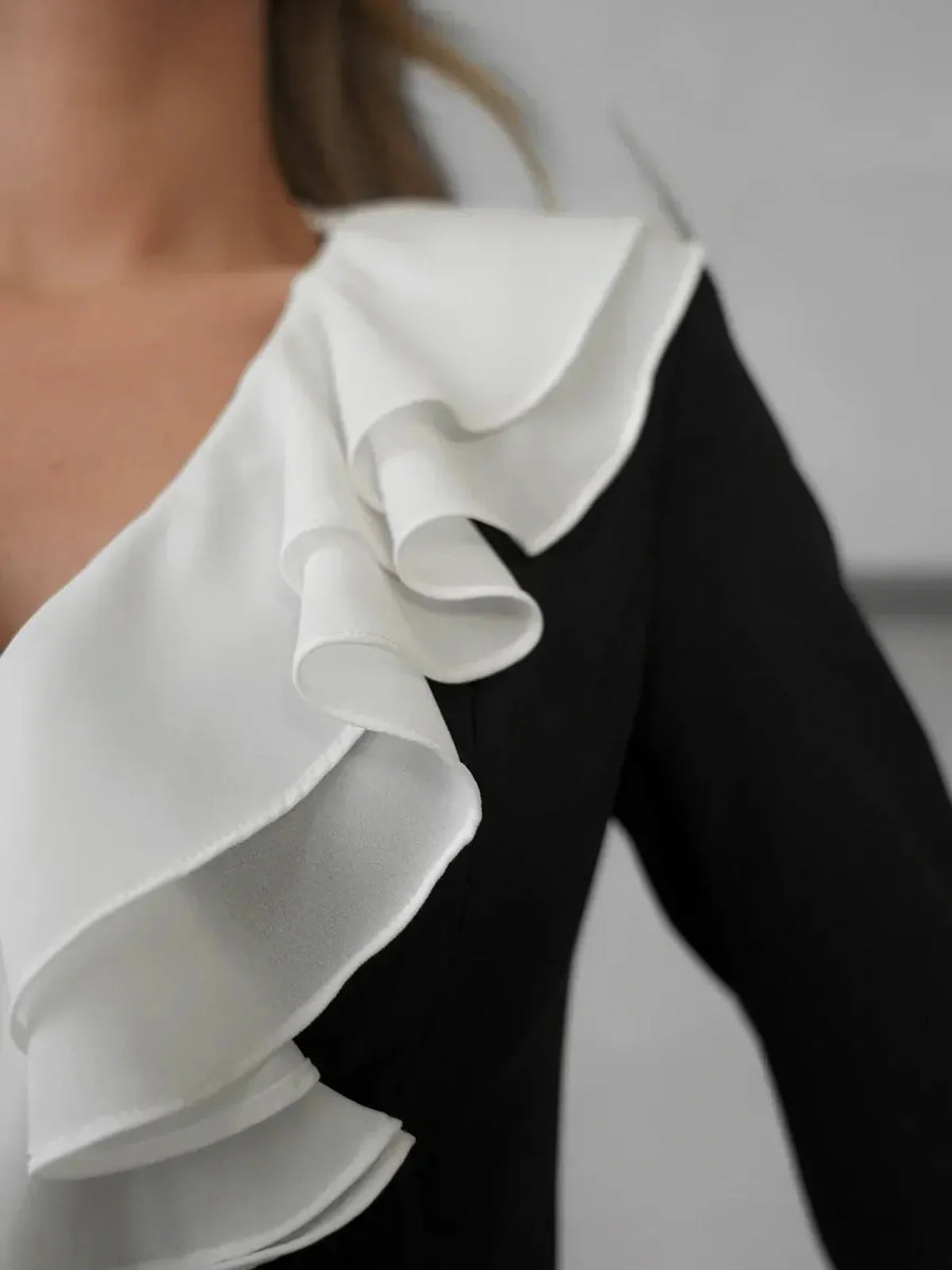 Close-up of black Velvet Fold Mini Dress featuring elegant white ruffle detail and deep V-neckline.