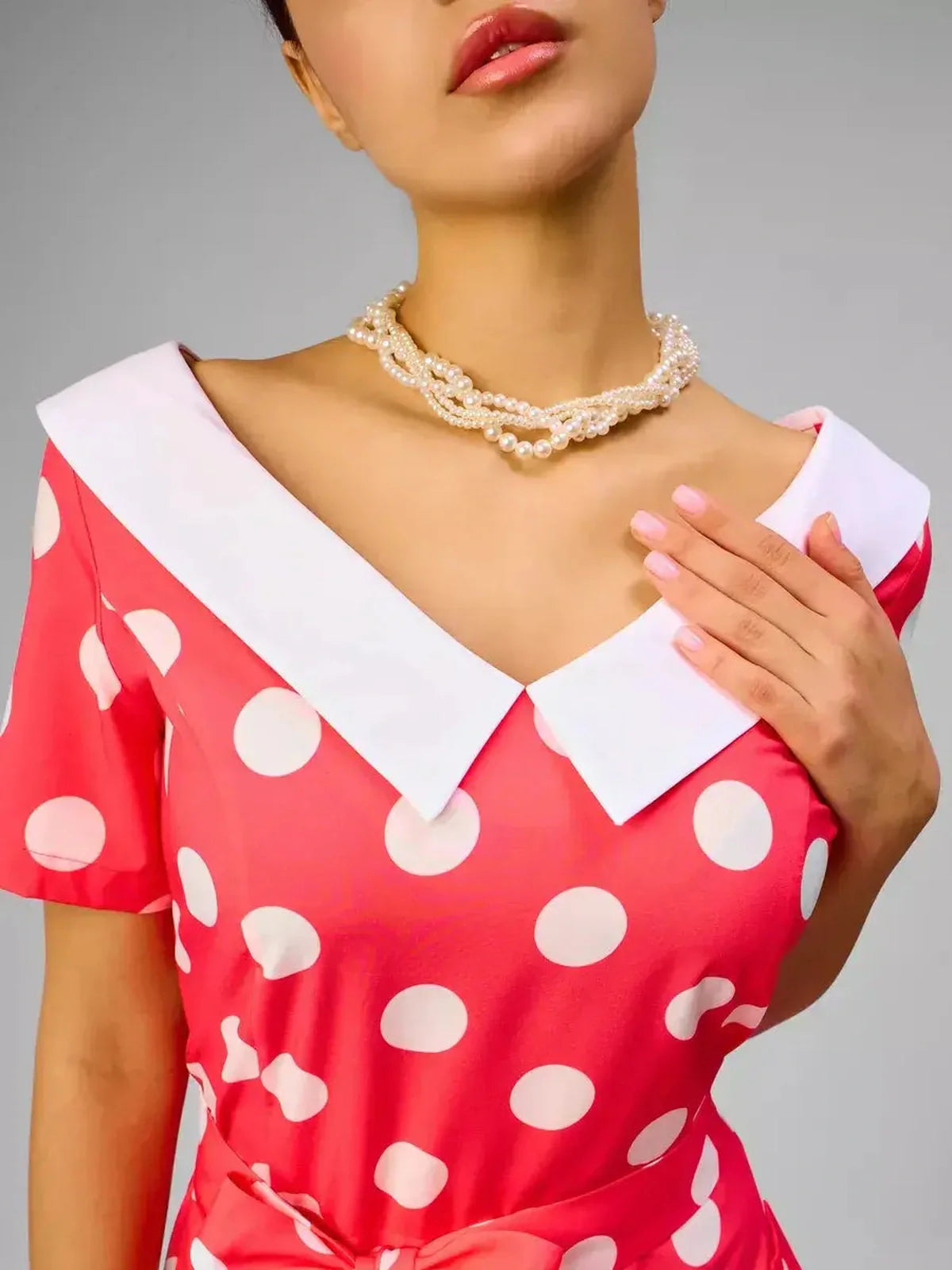 Close-up of a model wearing a Sailor Chic Midi Dress in pink with polka dots and a white sailor collar, accessorized with pearls.