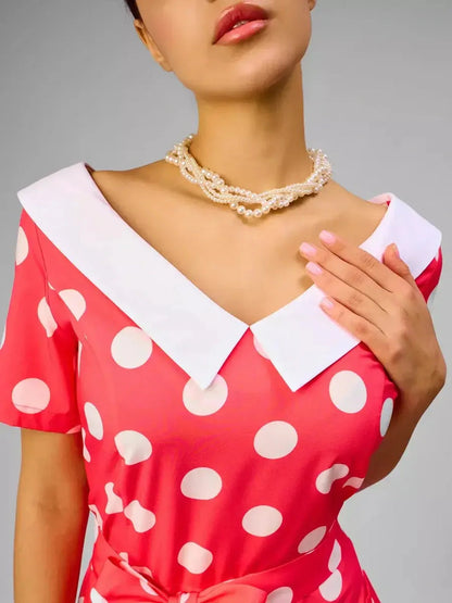 Close-up of a model wearing a Sailor Chic Midi Dress in pink with polka dots and a white sailor collar, accessorized with pearls.