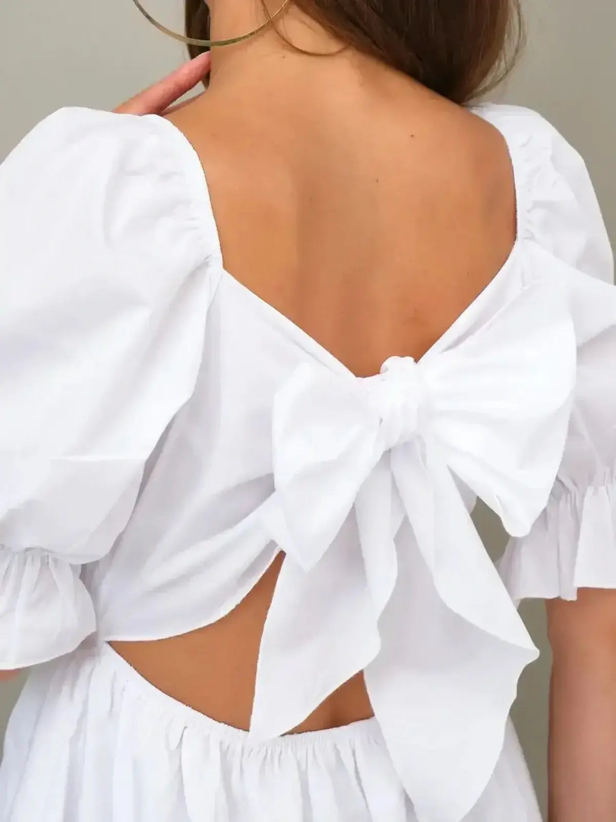 Back view of a white dress featuring a charming bow detail and puff sleeves, perfect for summer occasions.