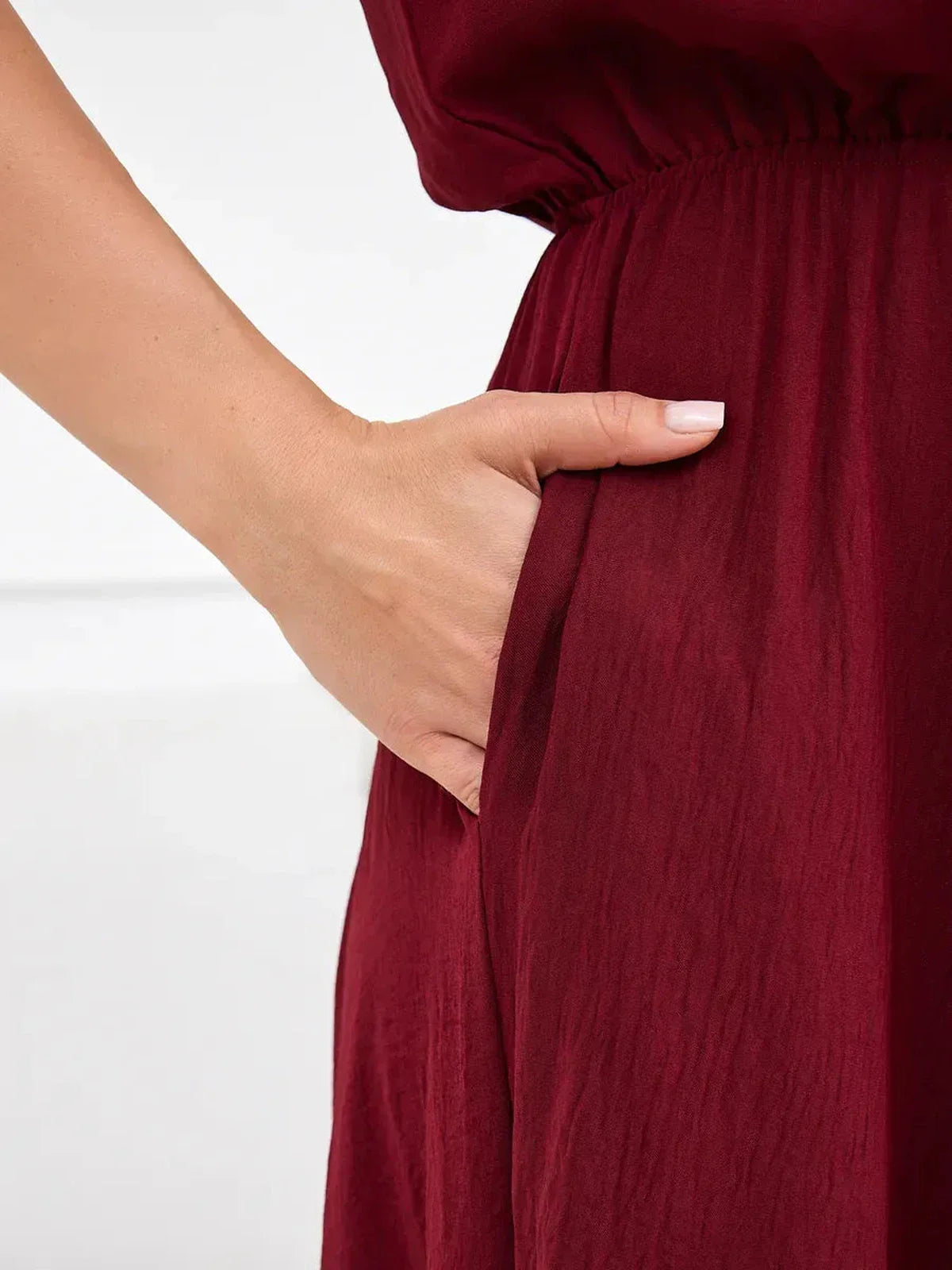 Close-up of a hand in the pocket of a burgundy maxi dress, highlighting the dress's stylish and functional design.